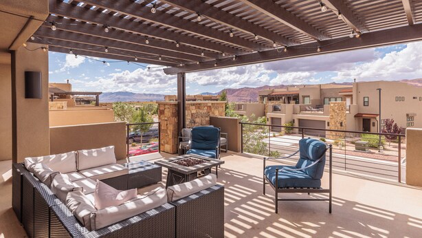 An outdoor patio with a grill, wicker furniture, and a view of the surrounding buildings and mountains. - Family 4BR Sleeps 23 - Private Hot Tub Near Pool (St. George)