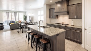 A modern kitchen with a large island, dark wood cabinets, and a dining area with a sofa and chairs. - Family 4BR Sleeps 23 - Private Hot Tub Near Pool (St. George)