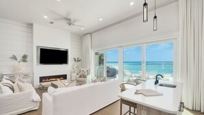 A modern living room with a fireplace, a large TV, and a view of the ocean.