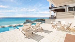 A poolside area with lounge chairs, a dining table, and a view of the ocean.