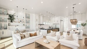 A spacious living area with white sofas and a wooden coffee table, a kitchen with white cabinets and a dining area with a wooden table and chairs.