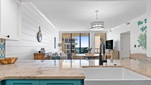Una cocina moderna con una isla grande, armarios blancos y vistas al área de estar.