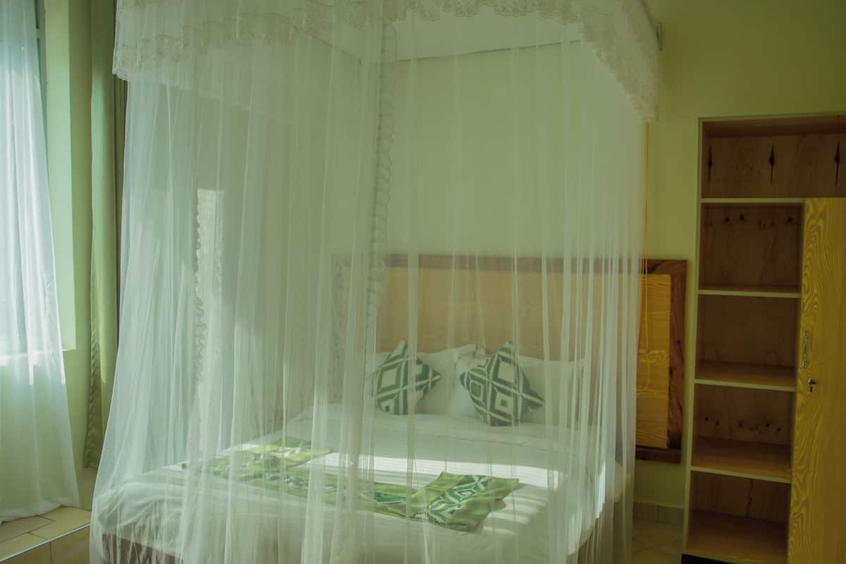 A room with a bed under a white canopy, a wooden wardrobe, and a window with sheer curtains.