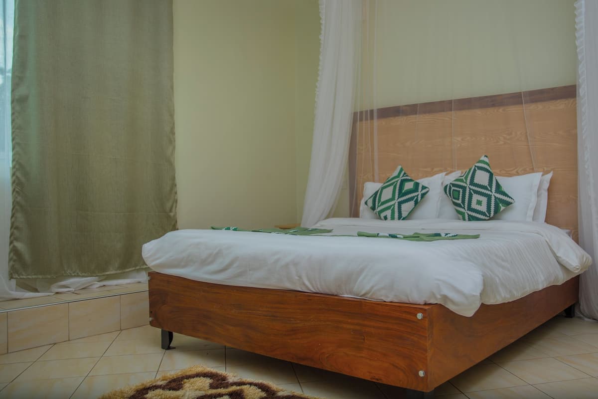 A wooden bed with white bedding and green patterned pillows, a wooden headboard, and a white curtain.