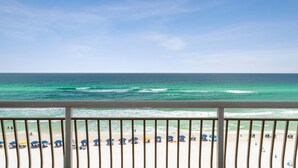 A beach view from a balcony with a railing, ocean waves, and beach umbrellas.