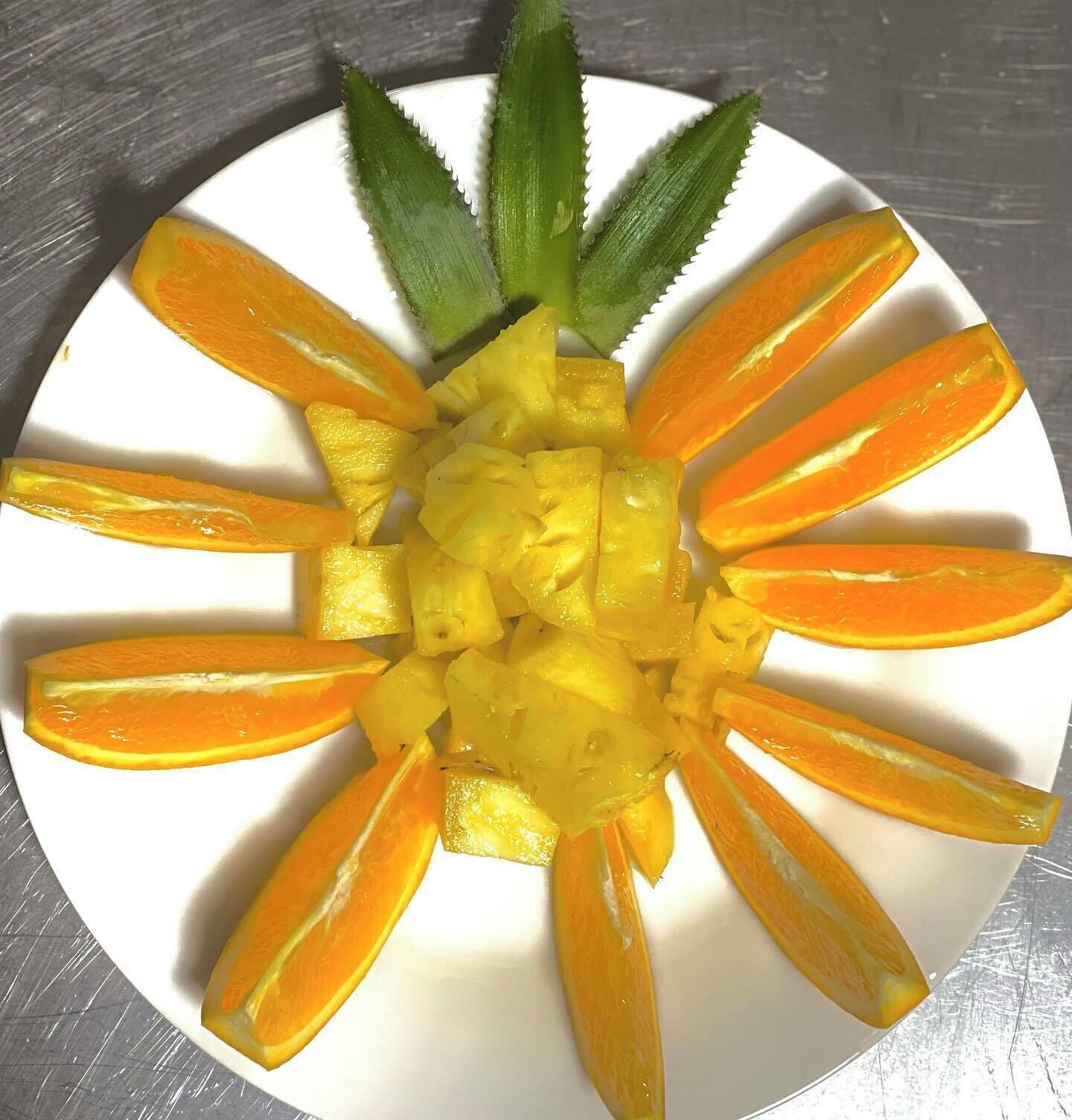 A white plate with a pineapple and orange slices arranged in a circular pattern.