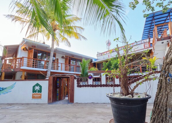 Un edificio de dos pisos con un balcón, una palmera y un letrero que indica Dhama Beach.