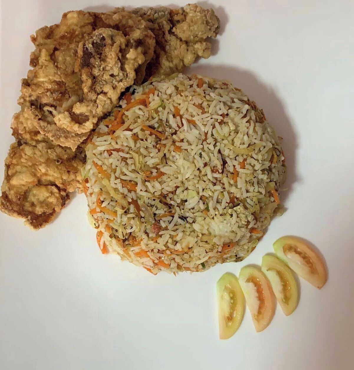 Un plato con pollo frito, arroz y rodajas de tomate.