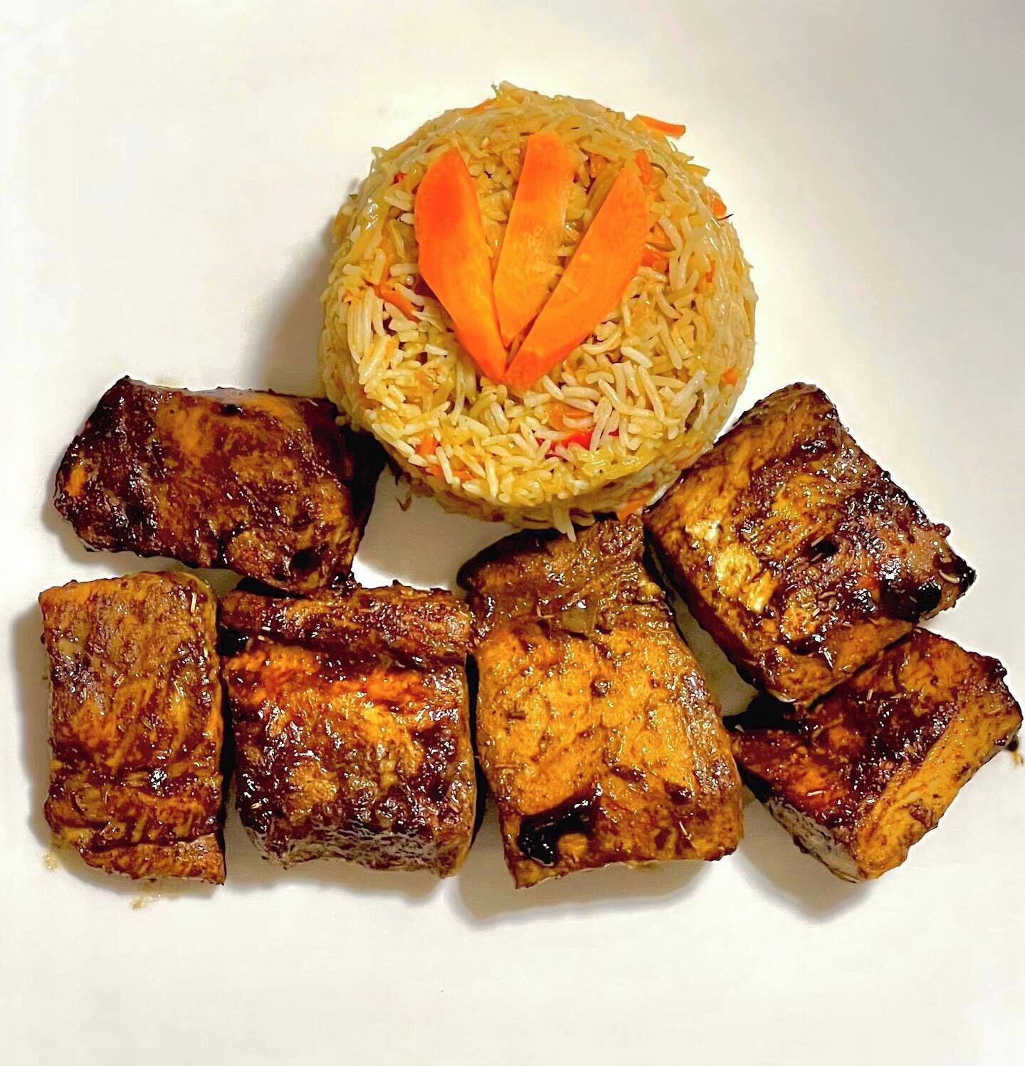 A plate with grilled meat and rice garnished with carrot slices.