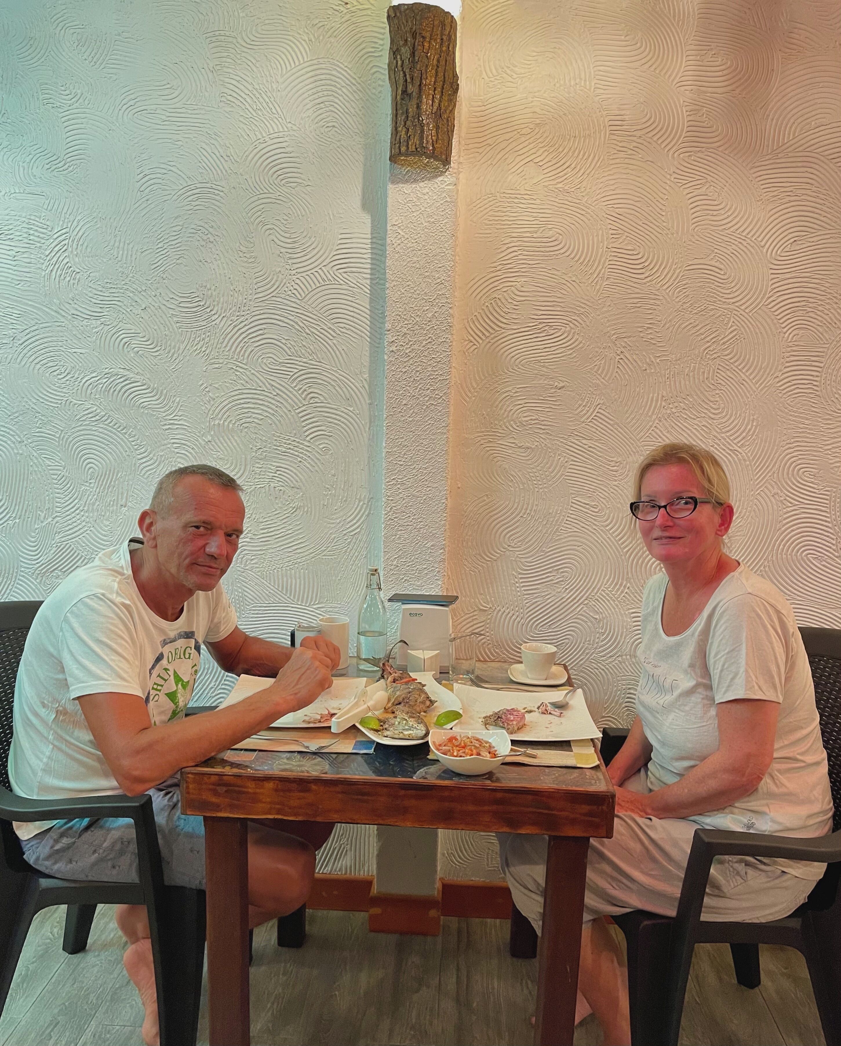 Two people seated at a table with plates of food, a bottle, and a cup.