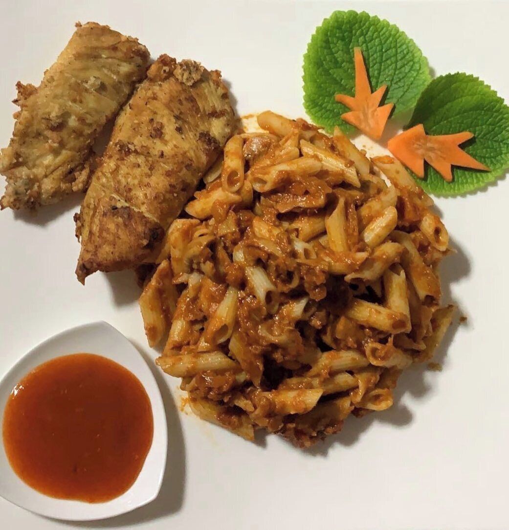 A plate with fried chicken, pasta, and a small bowl of sauce.