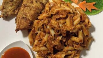 A plate with fried chicken, pasta, and a small bowl of sauce.
