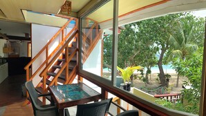 Une pièce avec un escalier en bois, une table en verre et une vue sur une plage bordée de palmiers.