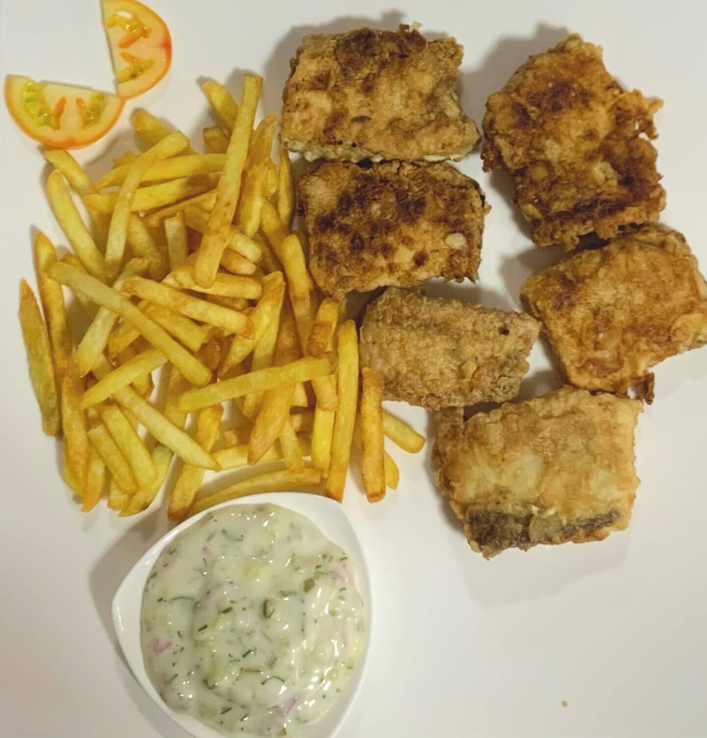 Un plato con pescado frito, papas fritas y un pequeño recipiente con salsa tártara.