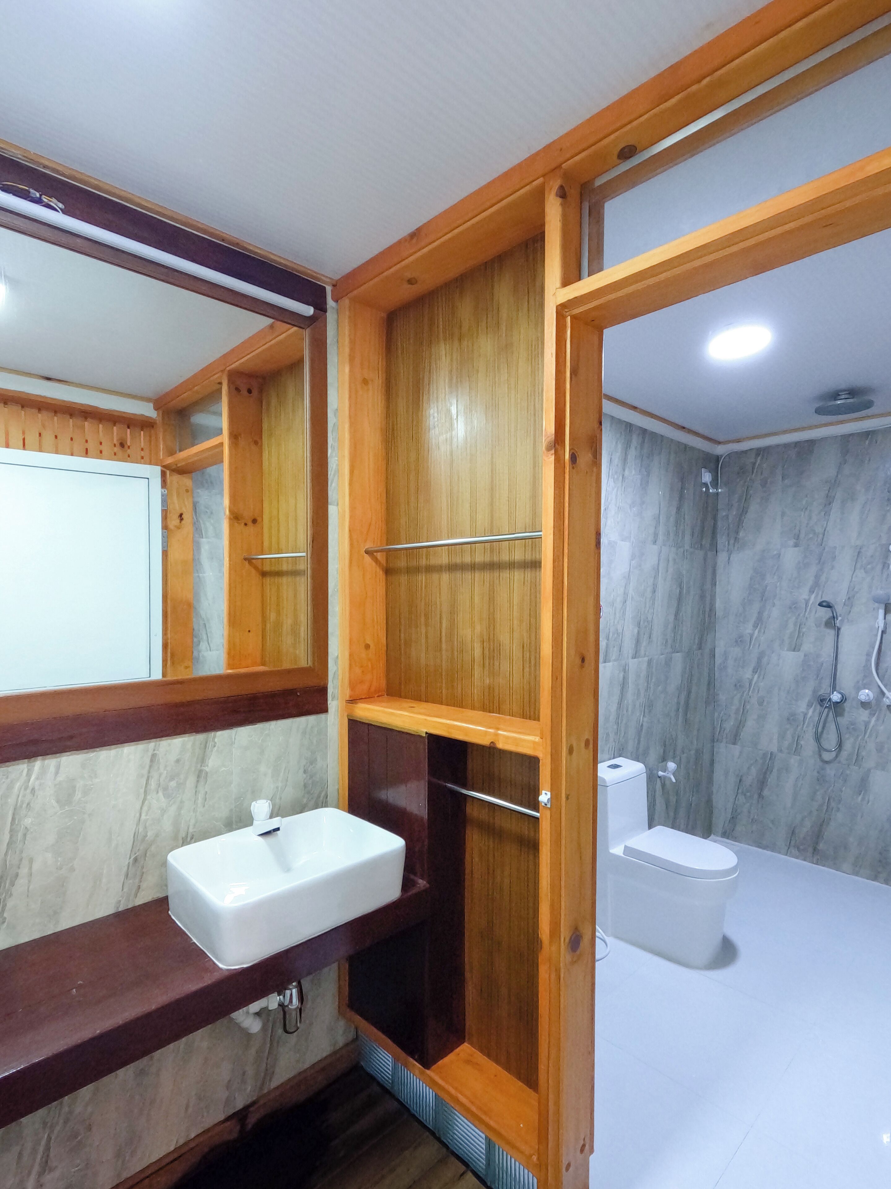A bathroom with a wooden vanity, a white sink, a mirror, and a shower area with a marble wall.