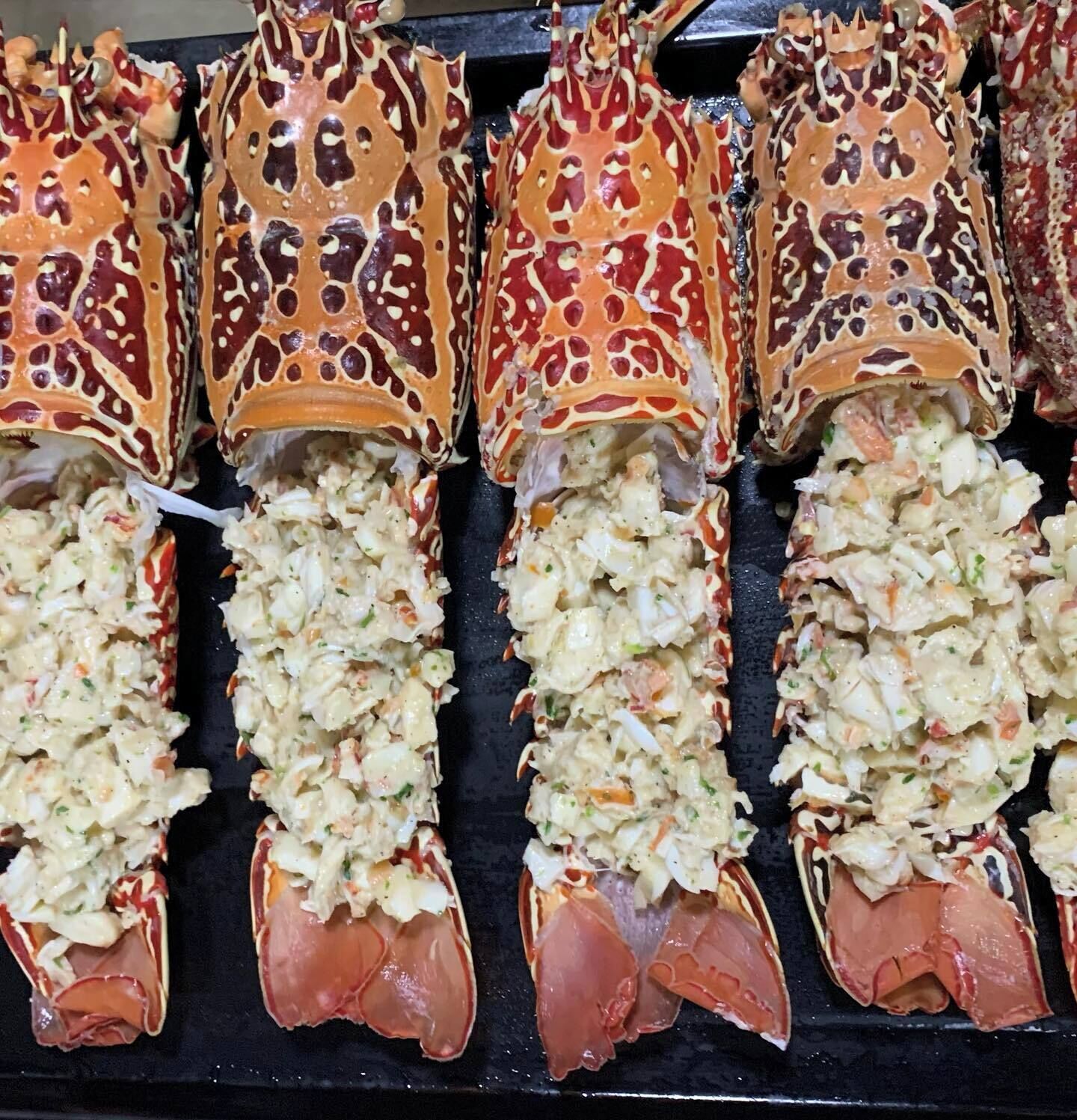 Lobsters with a creamy filling, likely a seafood salad, displayed on a black surface.