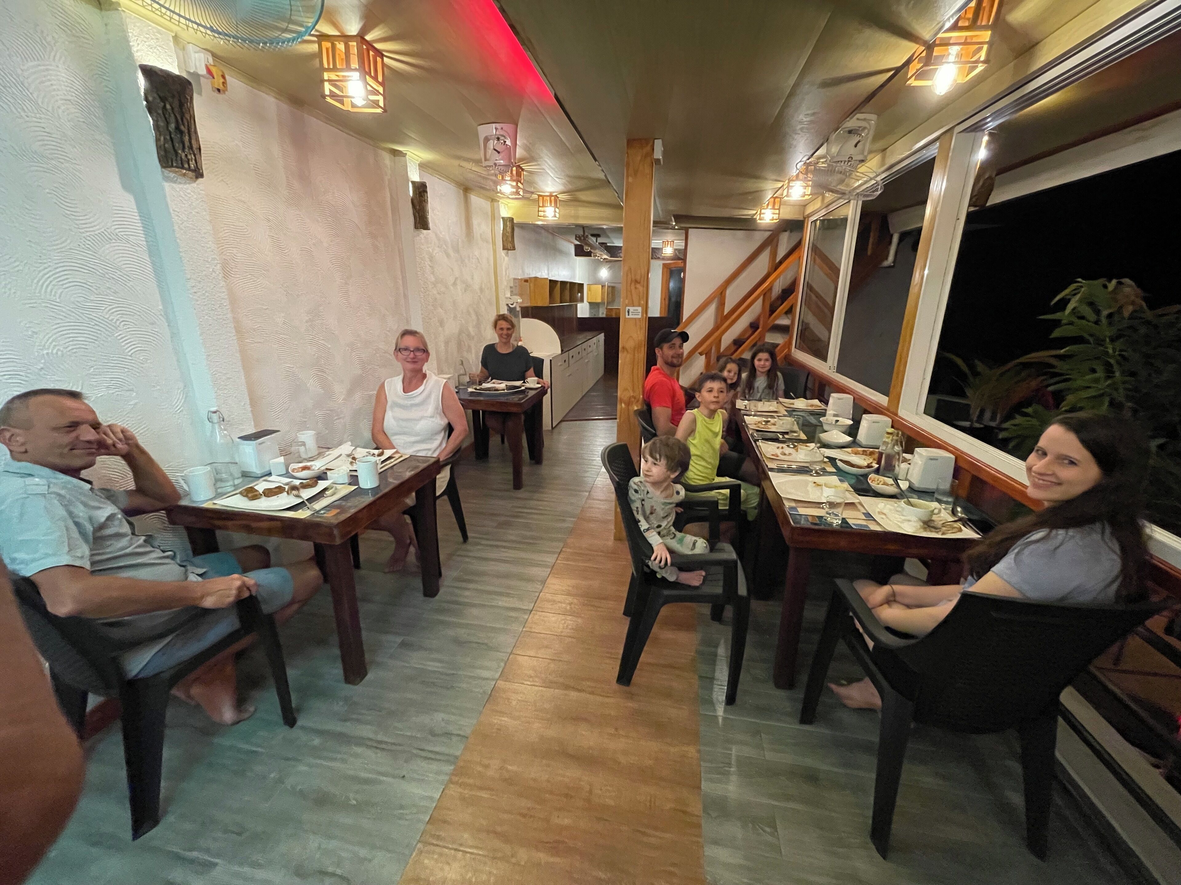 Un comedor con mesas y sillas de madera, una escalera y vistas de la noche.