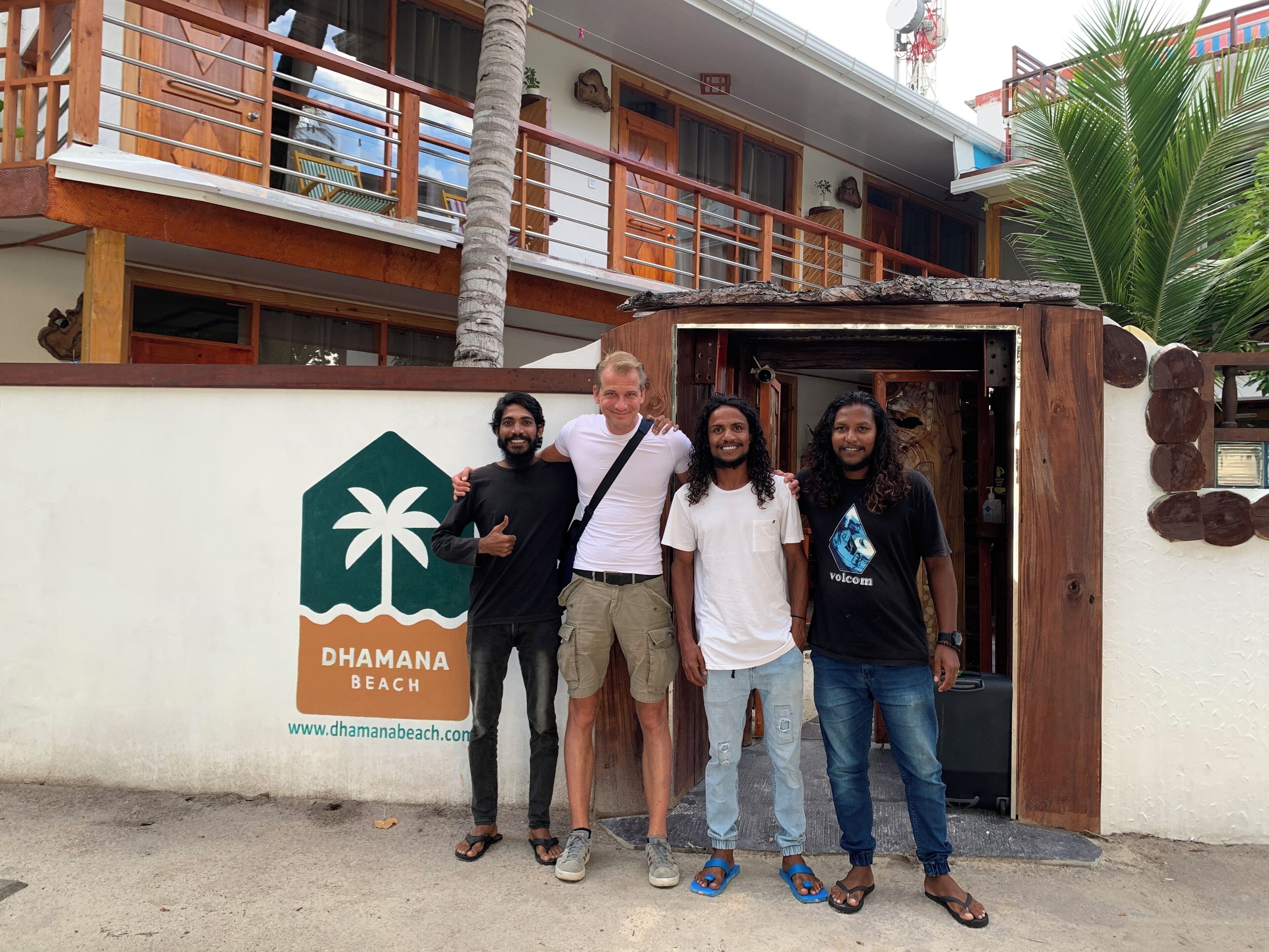 A group of people standing in front of a building with a sign reading "Dhamana Beach".