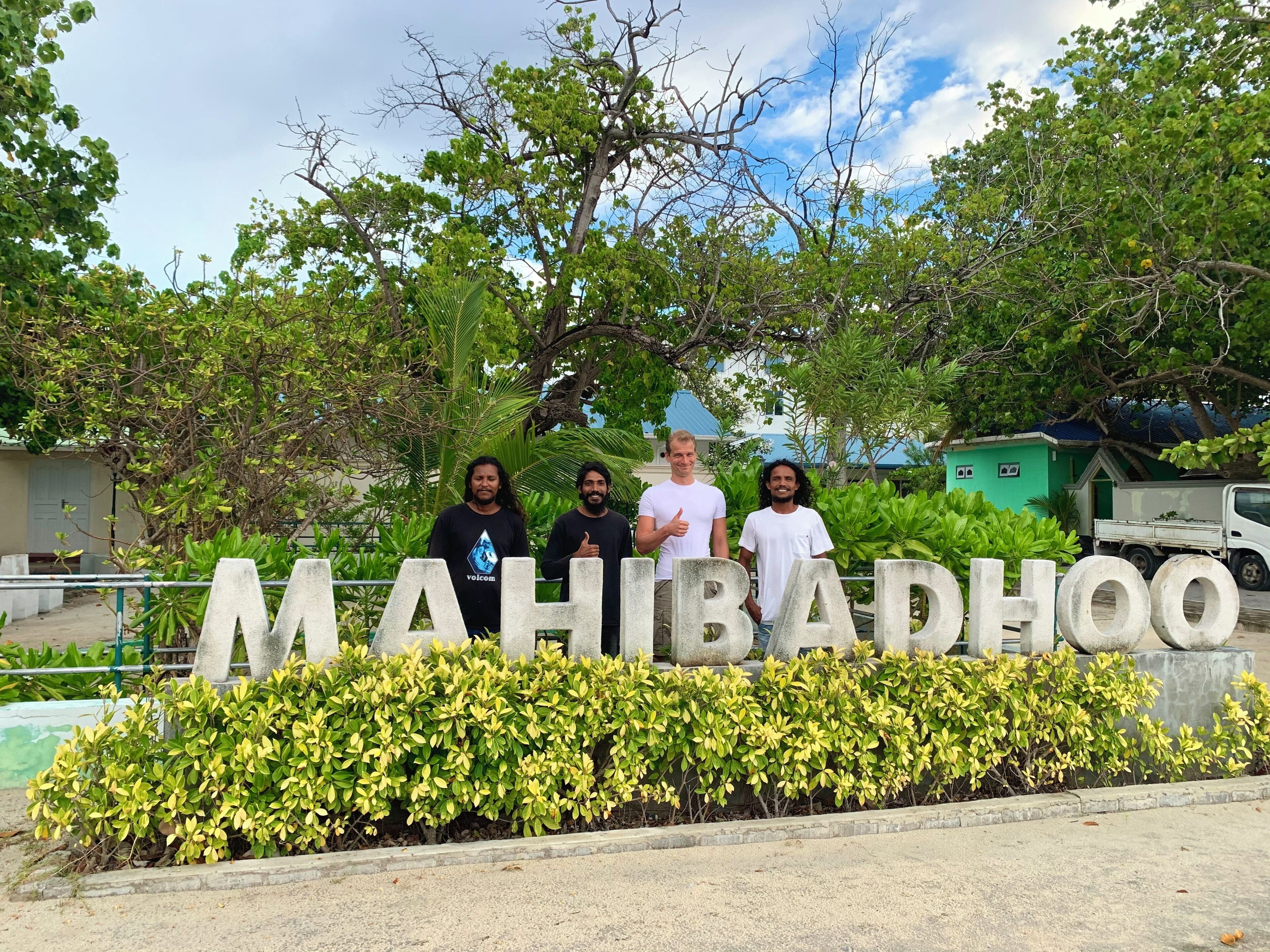 Un groupe de personnes se tient devant un panneau sur lequel on peut lire le texte « MAHIDHUO ».