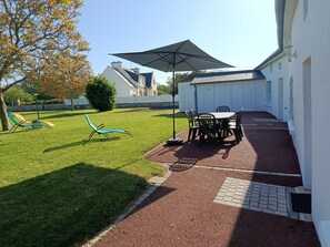 A patio area with a table and chairs, a lawn, and a building in the background. - Les Grands Embruns, Moins de 2 km des Plages (Moëlan-sur-Mer)