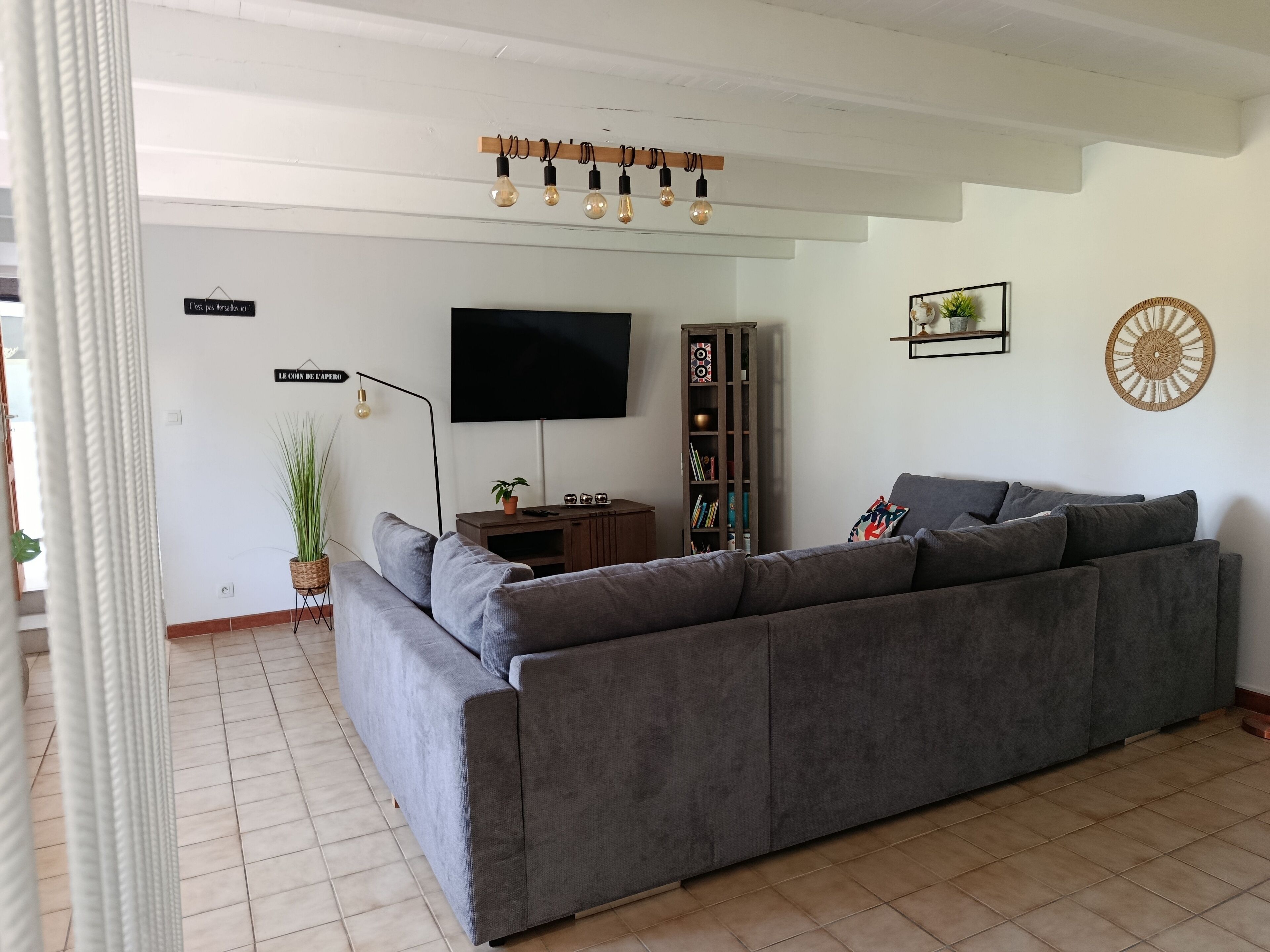 A living room with a grey sofa, a flat-screen TV, a tall bookshelf, and a decorative wall hanging.