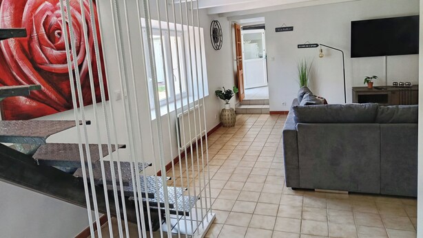 Un salon moderne avec un canapé gris, un téléviseur fixé au mur et un escalier doté d’une rampe blanche.