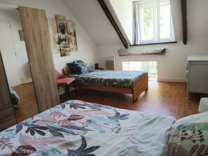 A bedroom with a wooden bed, a red chair, a window with curtains, and a Buddha statue on the wall. - Les Grands Embruns, Moins de 2 km des Plages (Moëlan-sur-Mer)