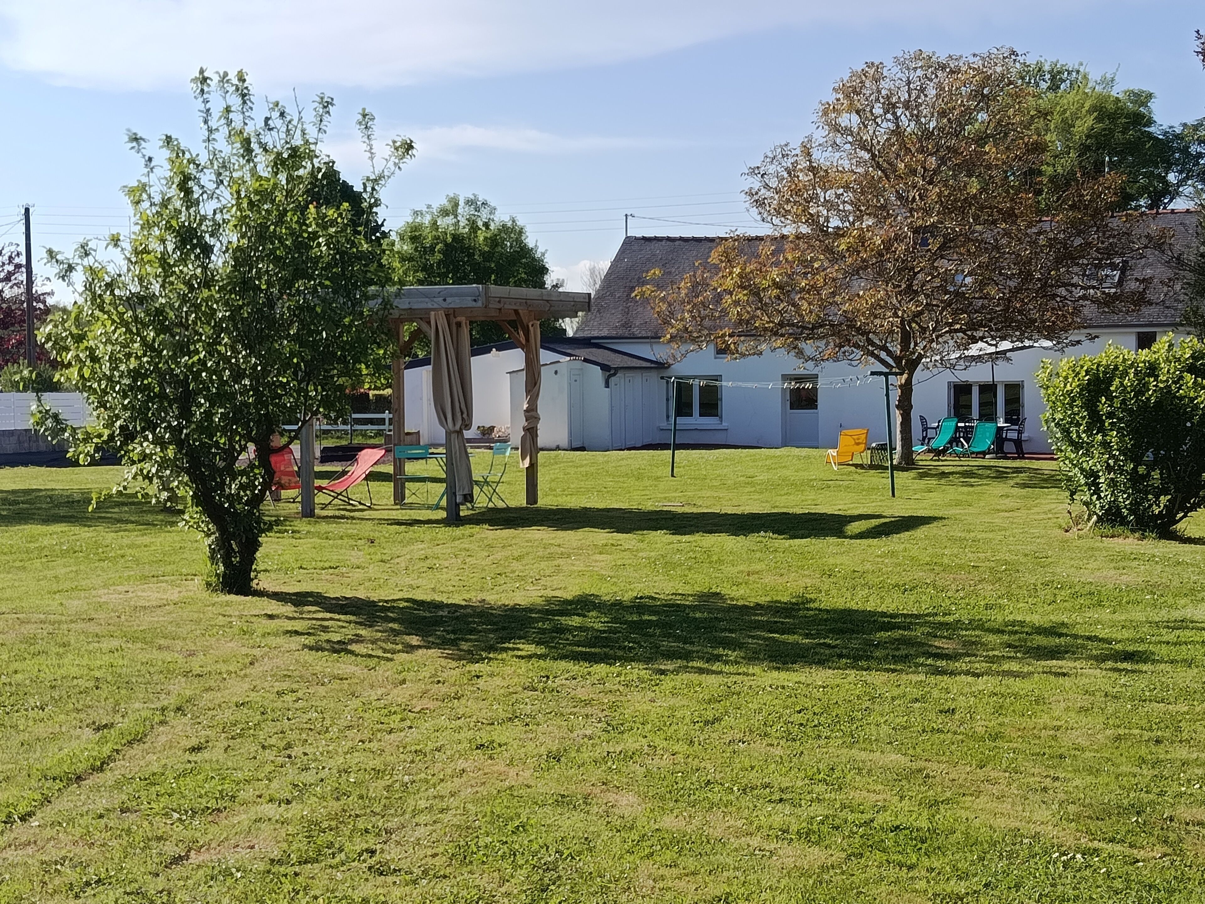 A grassy outdoor area with a swing set, a covered seating area, and a building with a white exterior in the background.