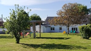 Un espace extérieur verdoyant avec une balançoire, un coin salon abrité et un bâtiment à l’arrière-plan dont la façade est blanche.