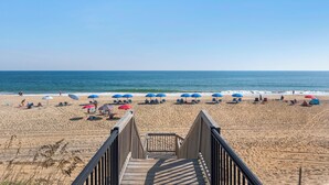 A wooden boardwalk leading to a beach with blue and red umbrellas. - Surfing Gecko: Oceanfront, Shared Pool, Dogs OK (Kill Devil Hills)