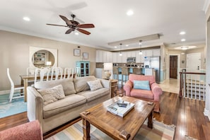 A spacious living room with a beige sofa, a wooden coffee table, and a pink armchair. A ceiling fan and recessed lighting are visible. - Surfing Gecko: Oceanfront, Shared Pool, Dogs OK (Kill Devil Hills)