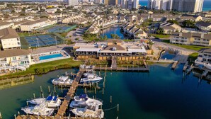 A marina with multiple boats docked, a restaurant with outdoor seating, and a view of the surrounding residential area and ocean. - Sandpiper Cove #9224 | Across from the Beach | Snowbird Friendly (Destin)