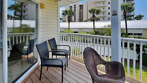 A balcony with wicker chairs, a glass door, and a view of high-rise buildings. - Sandpiper Cove #9224 | Across from the Beach | Snowbird Friendly (Destin)