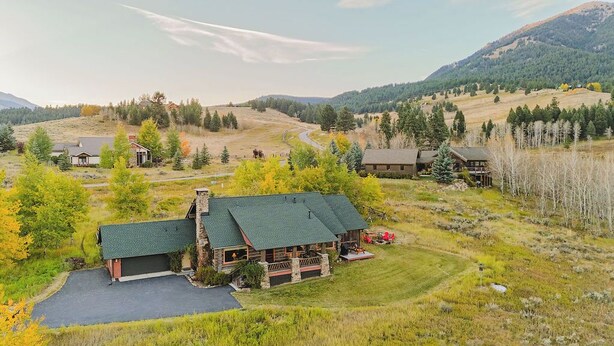 A lodge with a stone facade, a green roof, and a porch with outdoor seating. - Big Sky Vacation Rentals: Chief Joseph Log Home (Big Sky)