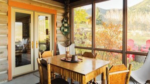 A wooden cabin with a dining area, large windows, and a view of the outdoors. - Big Sky Vacation Rentals: Chief Joseph Log Home (Big Sky)