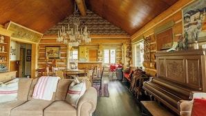 A log cabin interior with a wooden ceiling, a chandelier, a piano, and a dining area. - Big Sky Vacation Rentals: Chief Joseph Log Home (Big Sky)