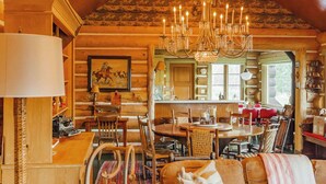 A cozy log cabin interior with a dining area, a chandelier, and a fireplace. - Big Sky Vacation Rentals: Chief Joseph Log Home (Big Sky)