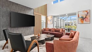 A modern living room with a sectional sofa, a black leather chair, and a flat-screen TV mounted on a textured wall. - The Marvelous | Brand NEW home w toy theme RM, pool, grand LR/DR, near Universal (Orlando)