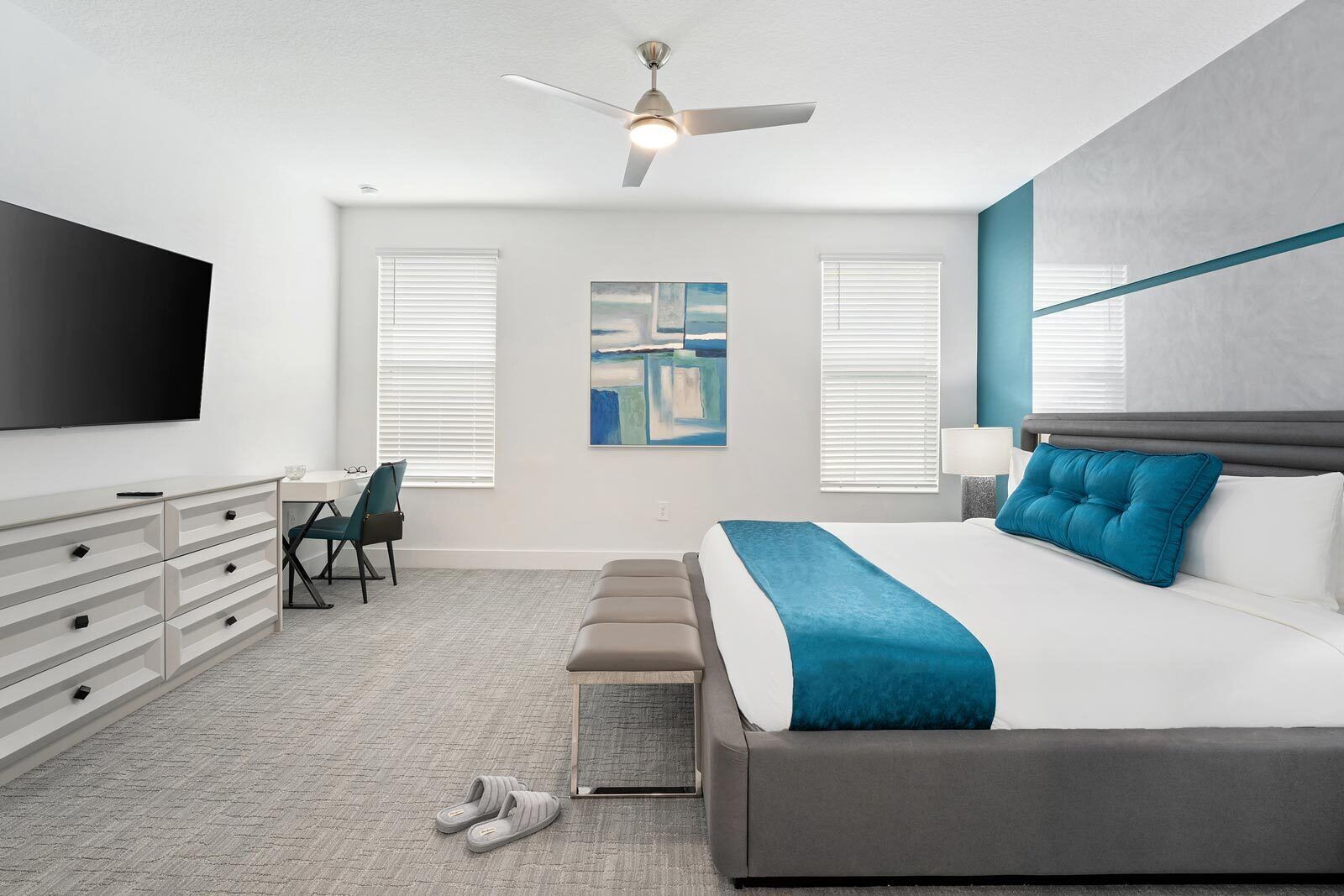 Une chambre moderne comprenant un lit, un bureau, une chaise, un téléviseur et un ventilateur de plafond.