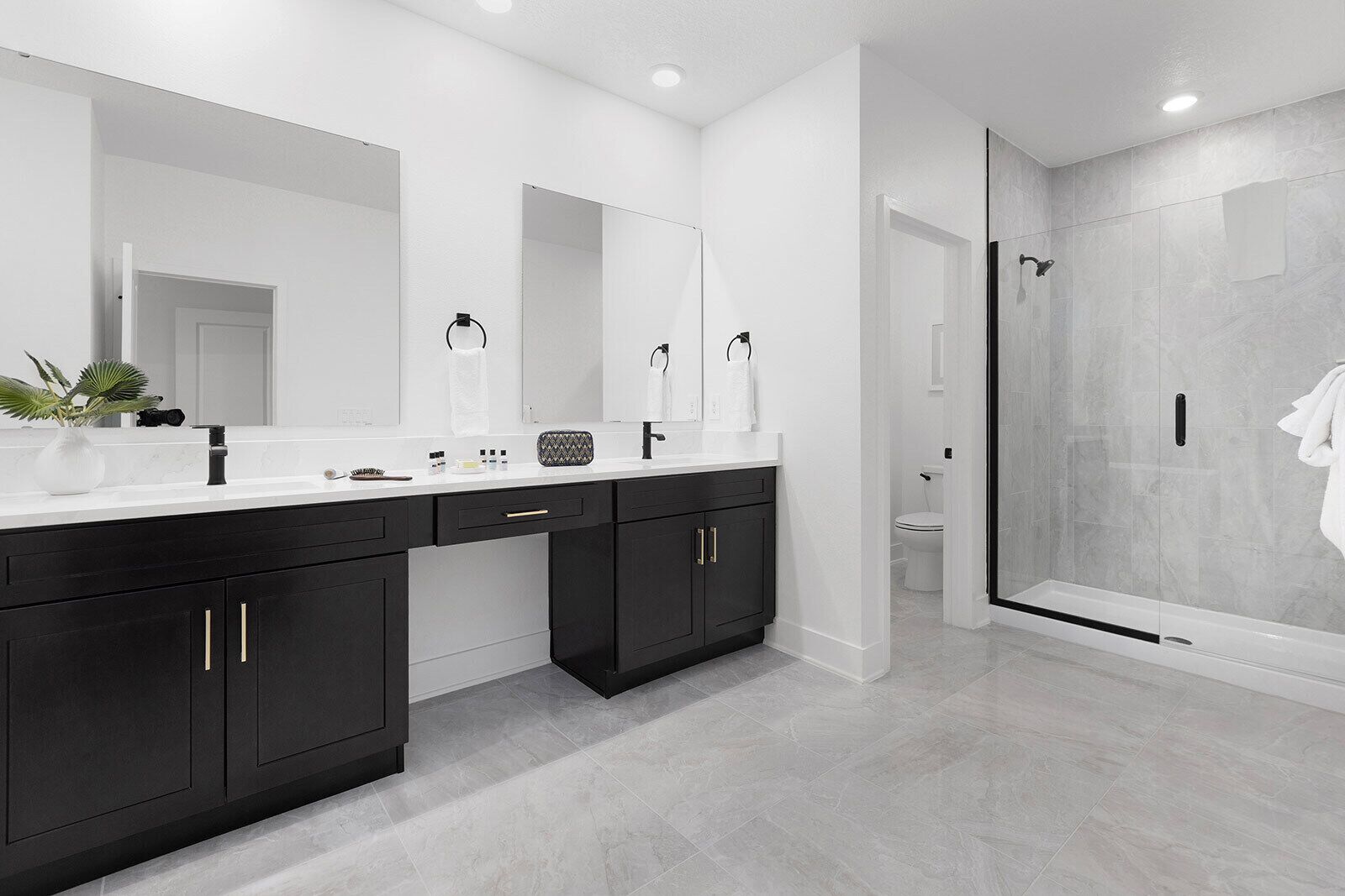 Un baño moderno con un espejo grande, muebles oscuros y una zona de ducha con paredes de vidrio.