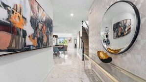 A hallway with marble flooring, a staircase, and modern art on the walls. - The Glorious | NEW designer home next to Universal ft. glam BRs, theme RMs, pool (Orlando)