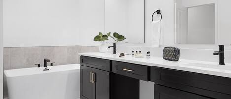 A modern bathroom with a white sink, black cabinets, and a large mirror.