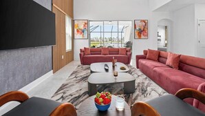 Uma sala de estar moderna com uma janela grande, dois sofás, uma mesa de centro e uma área de jantar com cadeiras.