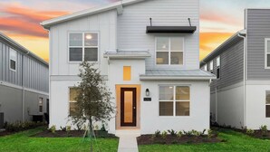 A two-story residential building with a modern design, featuring a prominent front door, a small porch, and a well-maintained lawn.