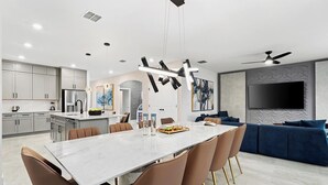 A modern kitchen with a dining area, a large TV, and a sofa.