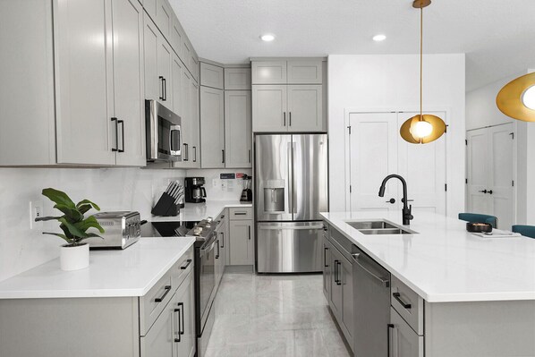 A modern kitchen with stainless steel appliances, white cabinetry, and a central island with a sink.
