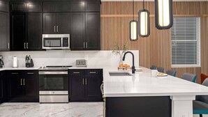 A modern kitchen with dark cabinetry, stainless steel appliances, a marble countertop, and a central island with seating.