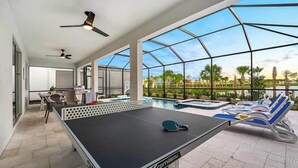 A ping pong table in a spacious indoor area with large windows, a pool, and lounge chairs.