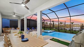 A modern outdoor dining area with a pool and a scenic view of a sunset over water. - Magnificent Mansion | Breathtaking estate mins to Universal, Disney, restaurants (Orlando)