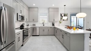 A modern kitchen with stainless steel appliances, grey cabinets, and a central island with breakfast items. - Magnificent Mansion | Breathtaking estate mins to Universal, Disney, restaurants (Orlando)